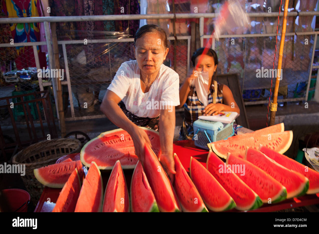 Une vieille femme vend des pastèques sur le marché indien à Yangon, Myanmar, la nuit, alors que sa fille essaie de décourager les mouches Banque D'Images