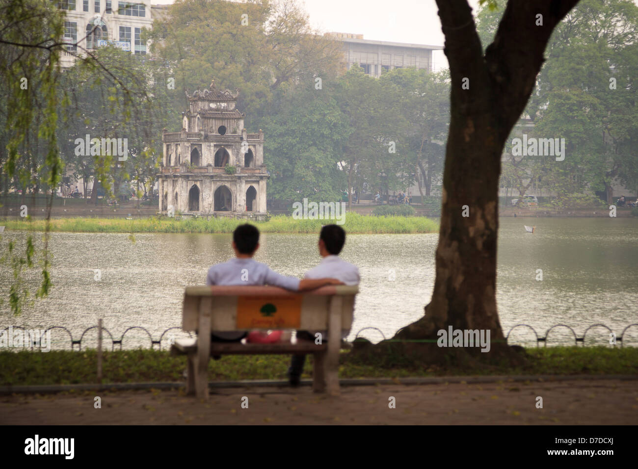 Deux hommes assis sur un banc avec vue sur le Tháp Rùa (Tortue) Tour sur Hoam Kiem, Hanoi, Vietnam Banque D'Images