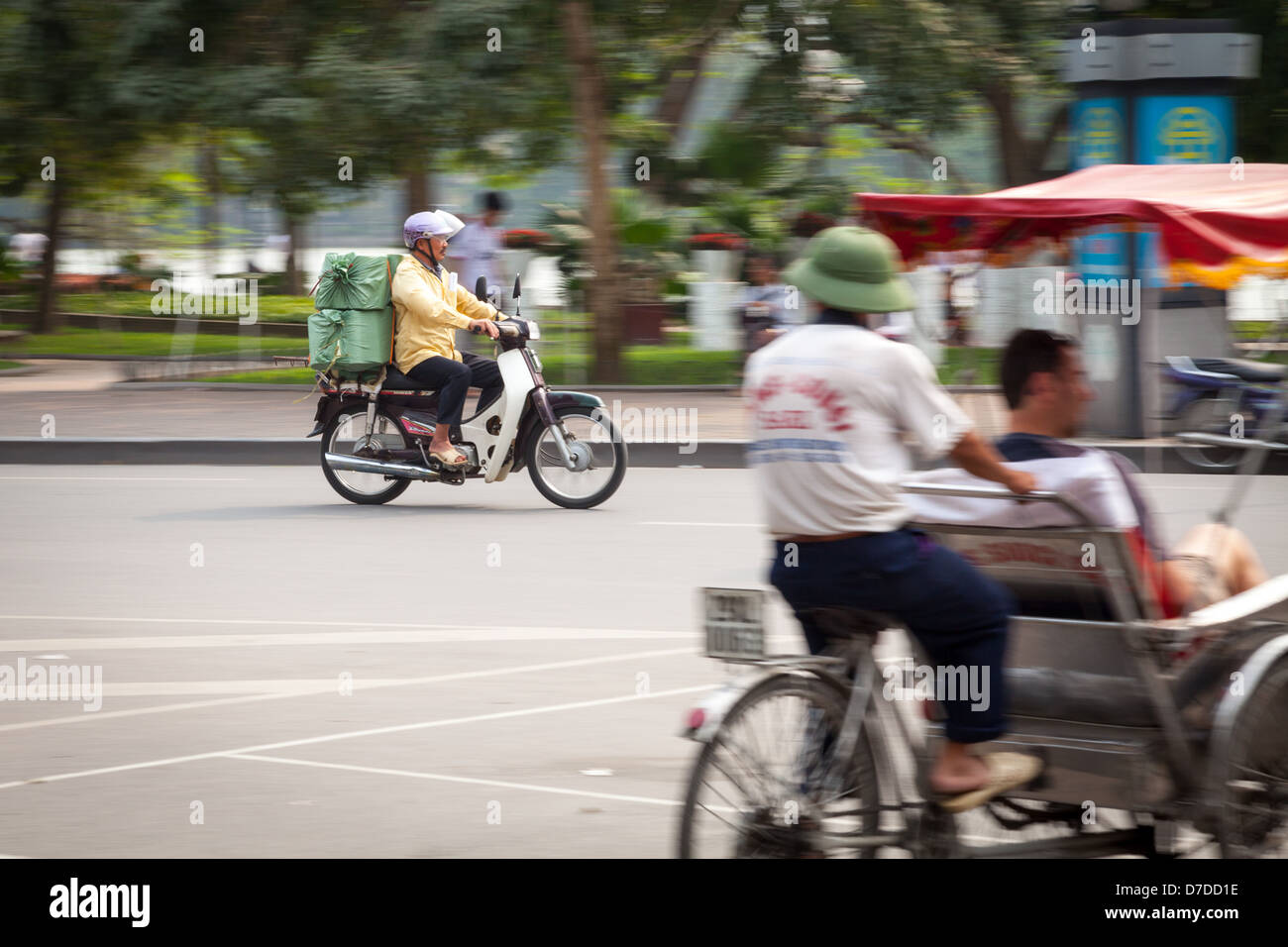 Un homme sur son scooter roulant passé Hoam Kiem et un pousse-pousse à Hanoi, Vietnam Banque D'Images