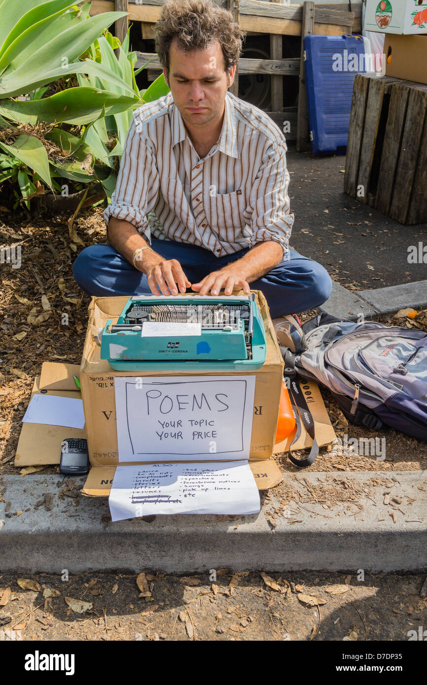 Un homme âgé de 25 à 30 ans est assis sur le sol avec sa machine à écrire Smith-Corona sur une boîte en carton d'origine vente de poèmes. Banque D'Images