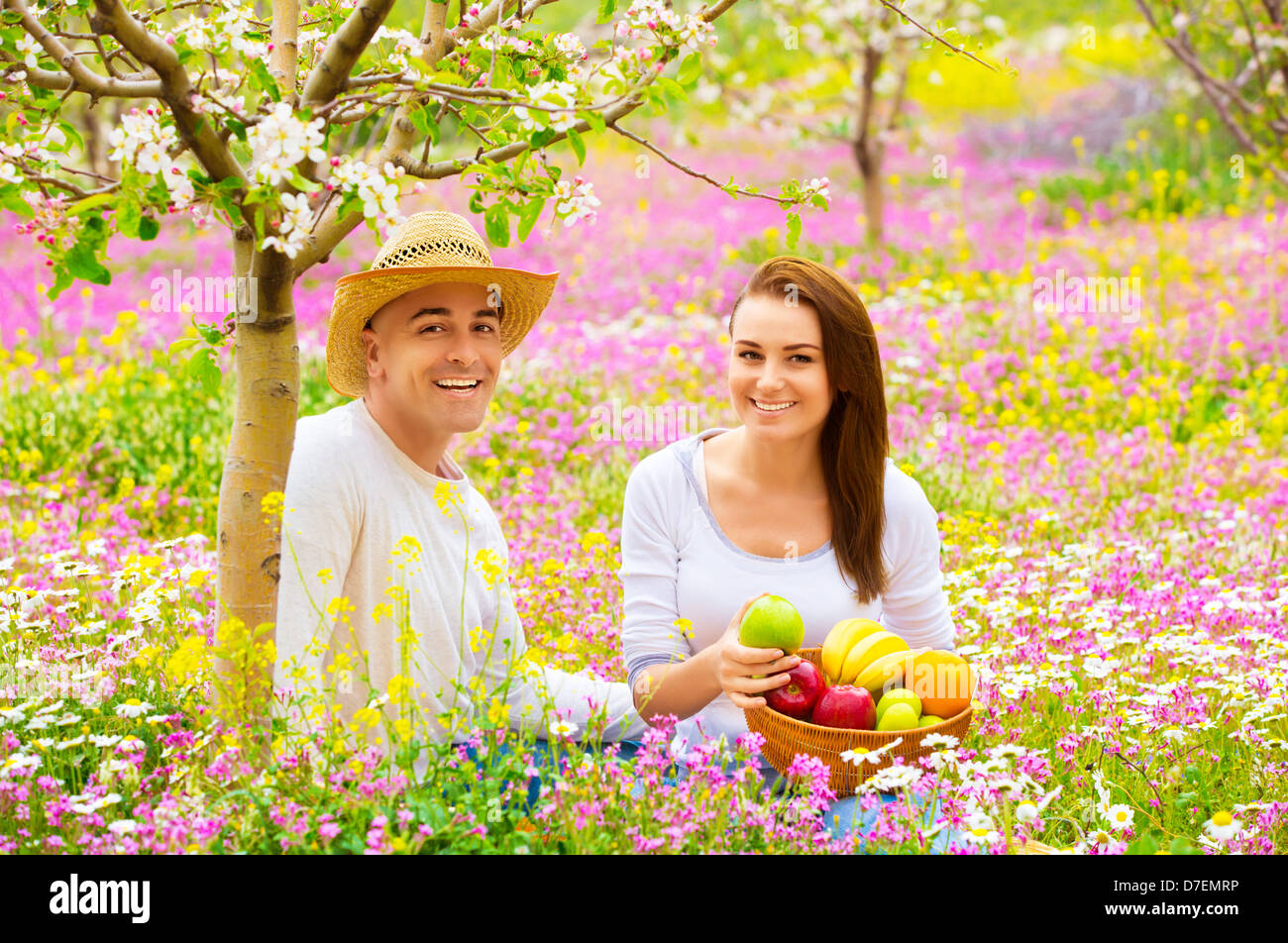 Happy smiling couple on pique-nique dans beau jardin en fleurs, manger de délicieux fruits frais, profiter de la nature printemps Banque D'Images