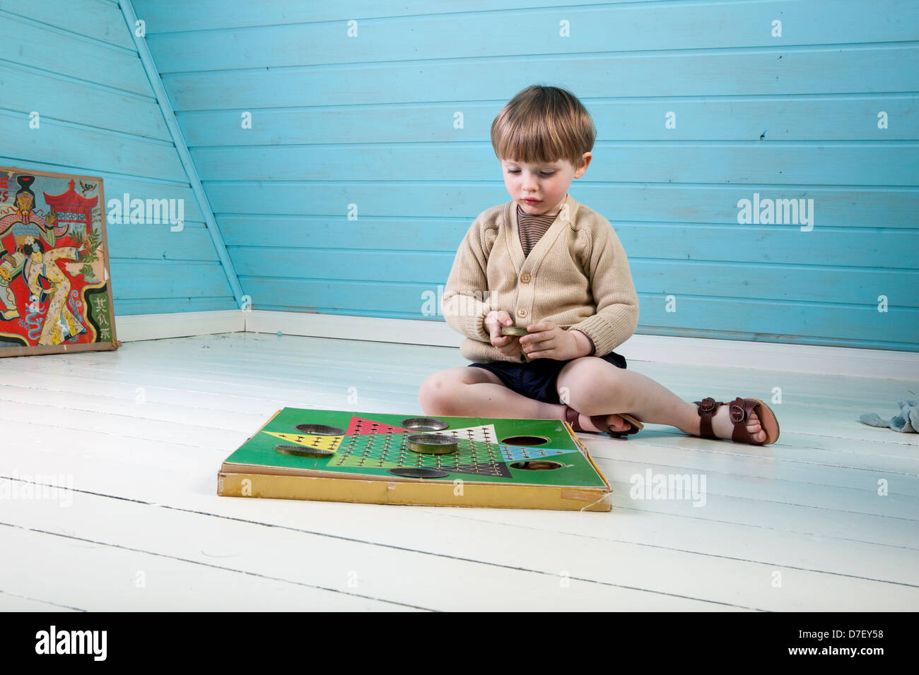 Un petit garçon dans de beaux vêtements et sandales est jouer seul avec jeu de bleu et blanc dans un loft. Banque D'Images