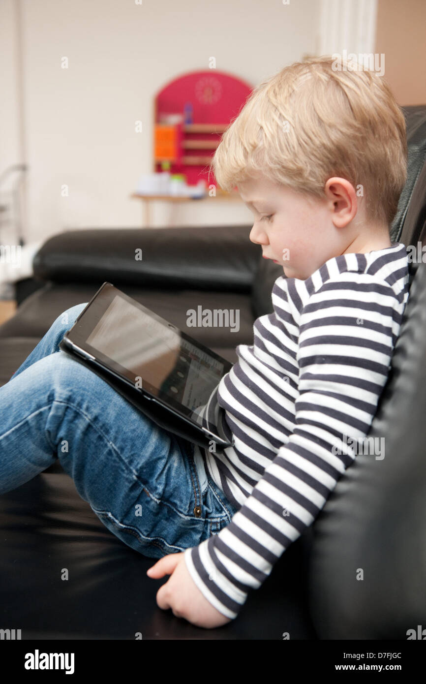 Un petit garçon est assis sur le canapé watchin quelque chose sur l'ipad. Banque D'Images