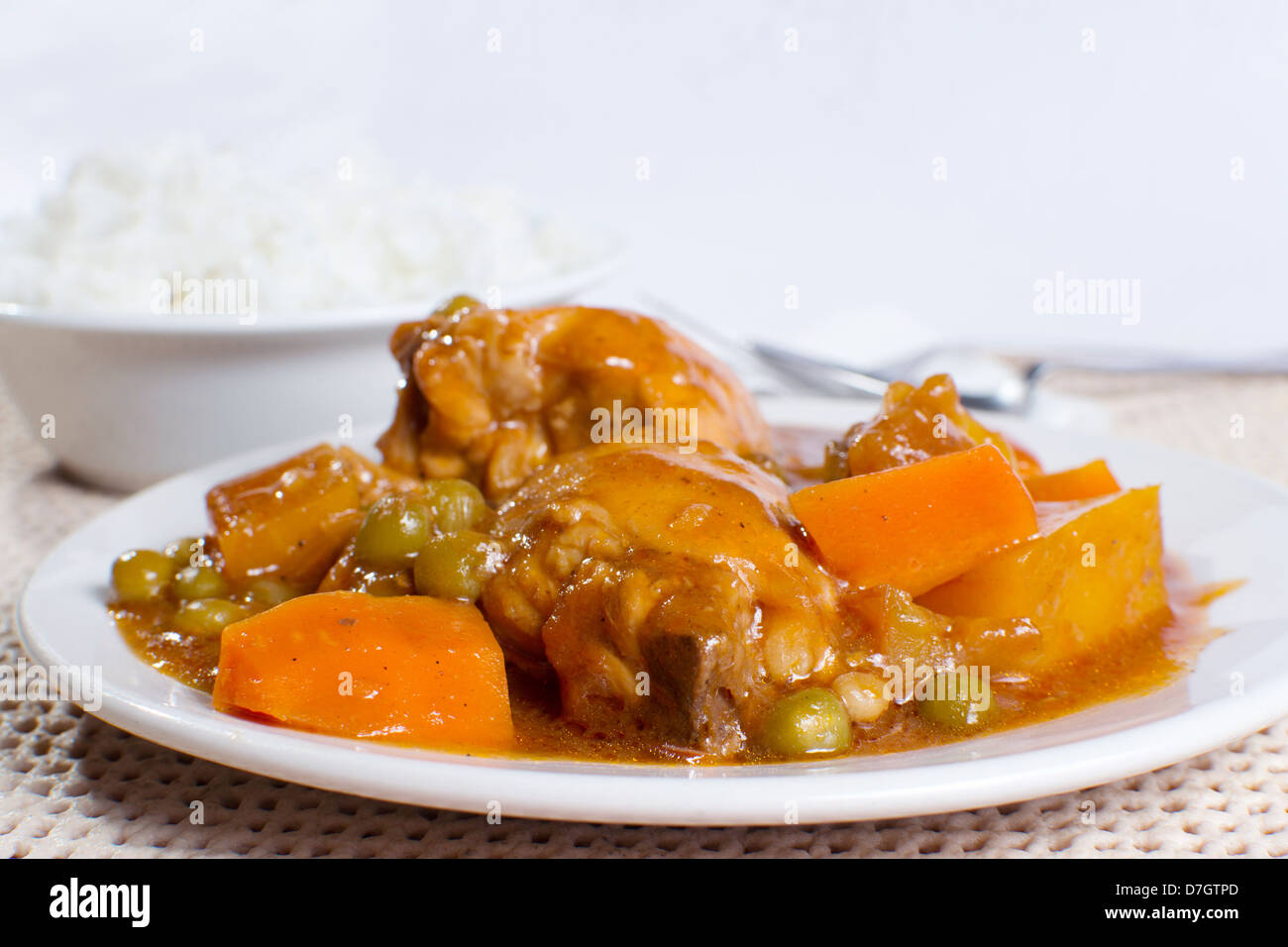 Une photo de ragoût de poulet avec pommes de terre, carottes, petits pois à la sauce tomate et le bol de riz étuvé Banque D'Images