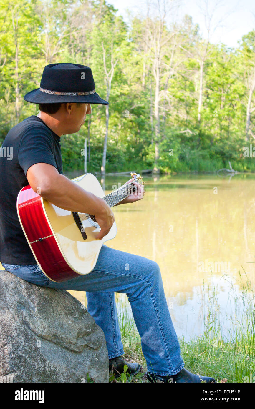 Un homme dans un chapeau de cow-boy joue une guitare acoustique vers  l'extérieur à un étang tranquille, à Sarnia, Ontario, Canada Photo Stock -  Alamy