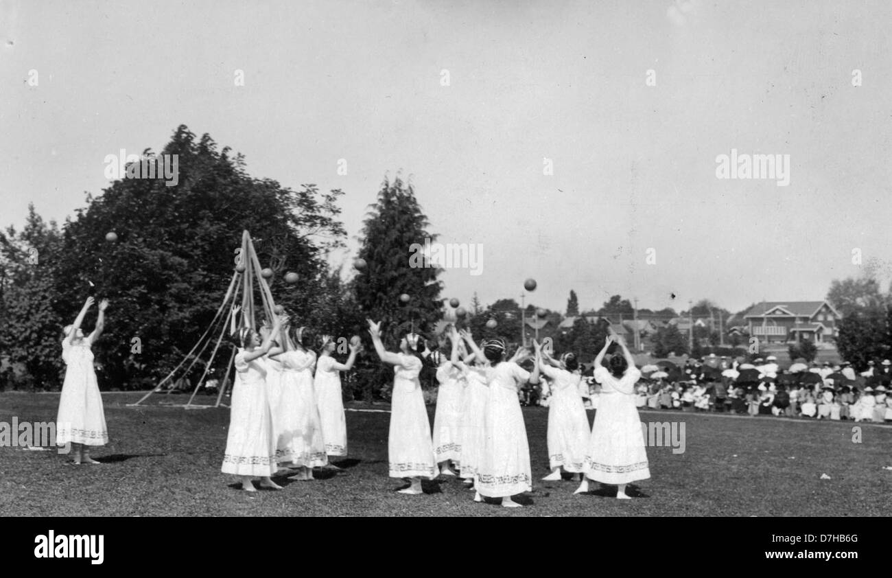 Une scène du concours du 1er mai montrant des jeunes filles grecques vêtues de robes blanches jouant au ballon, avec une danse Maypole en arrière-plan. Cet événement met en lumière les célébrations printanières traditionnelles, avec des performances symboliques associées au renouveau et à la fertilité. L’image fait partie de la collection des Archives de l’OSU, capturant l’essence des festivités saisonnières et des pratiques culturelles. Banque D'Images