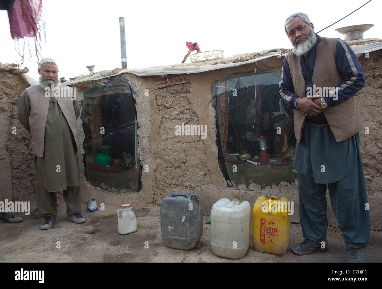 Deux réfugiés afghans devant leur maison de terre. Les fenêtres sont vieilles fenêtres de voiture. Banque D'Images