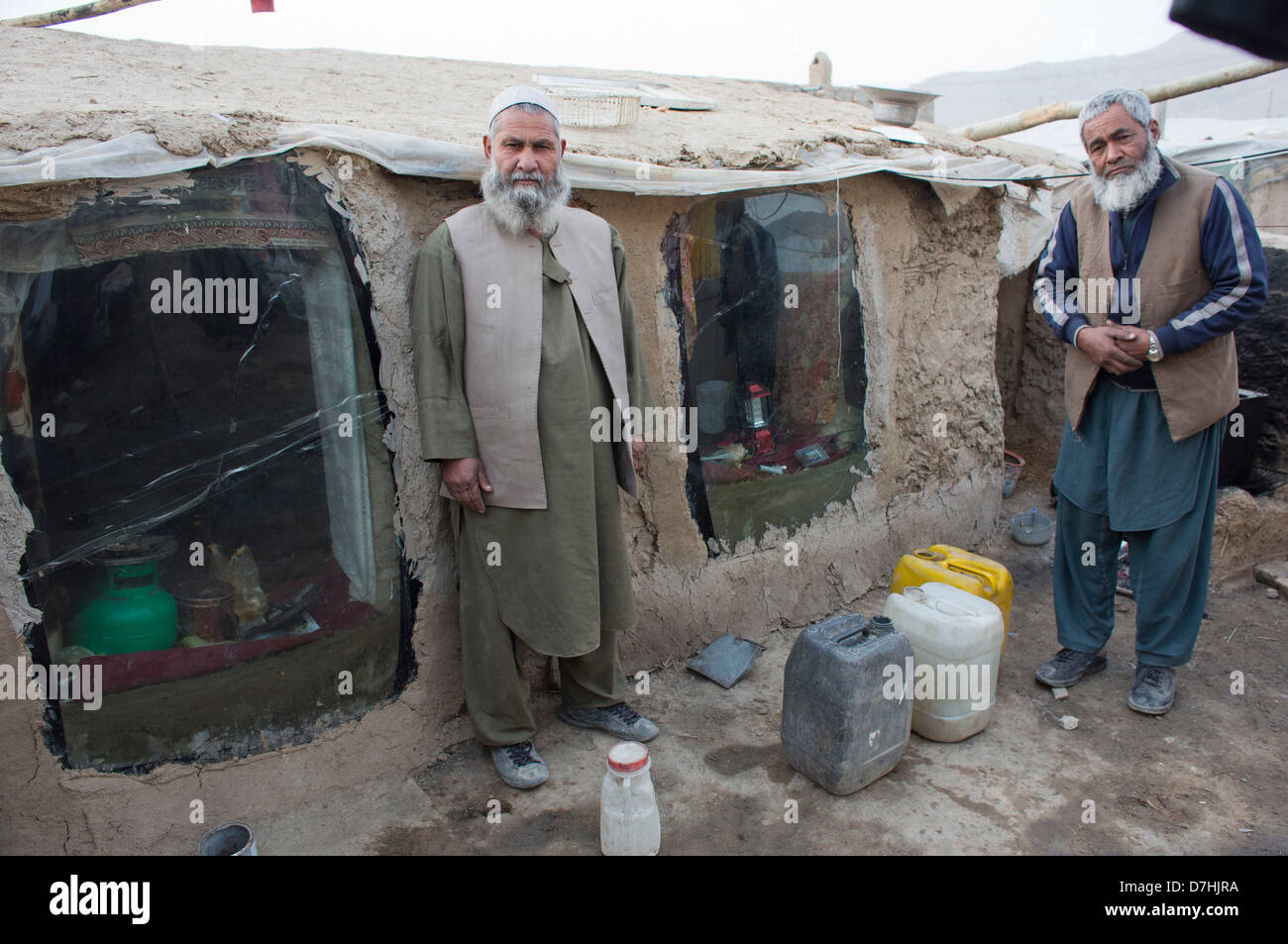 Deux réfugiés afghans devant leur maison de terre. Les fenêtres sont vieilles fenêtres de voiture. Banque D'Images