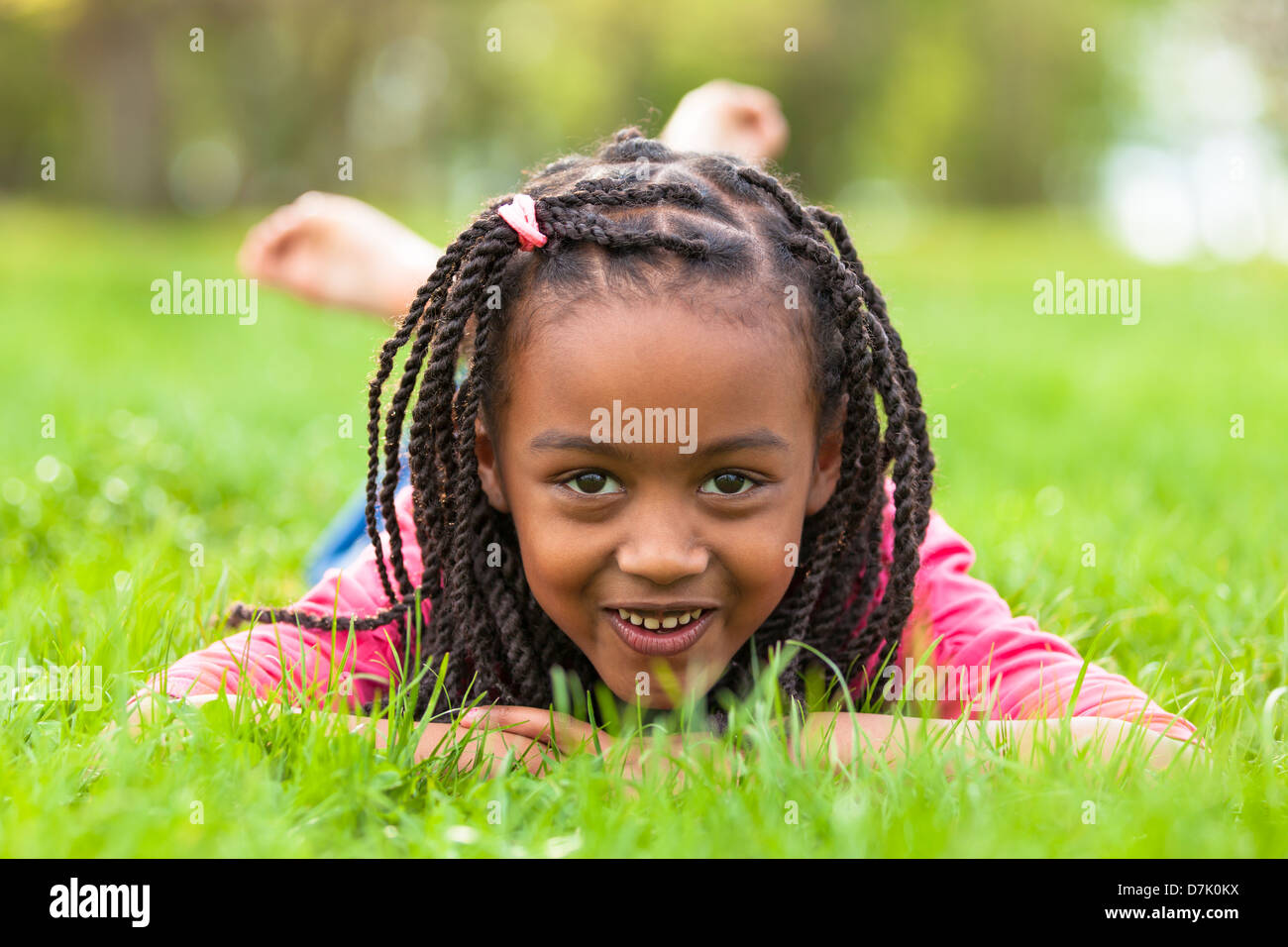 Outdoor portrait of a cute jeune fille noire couchée sur l'herbe et souriant - peuple africain Banque D'Images