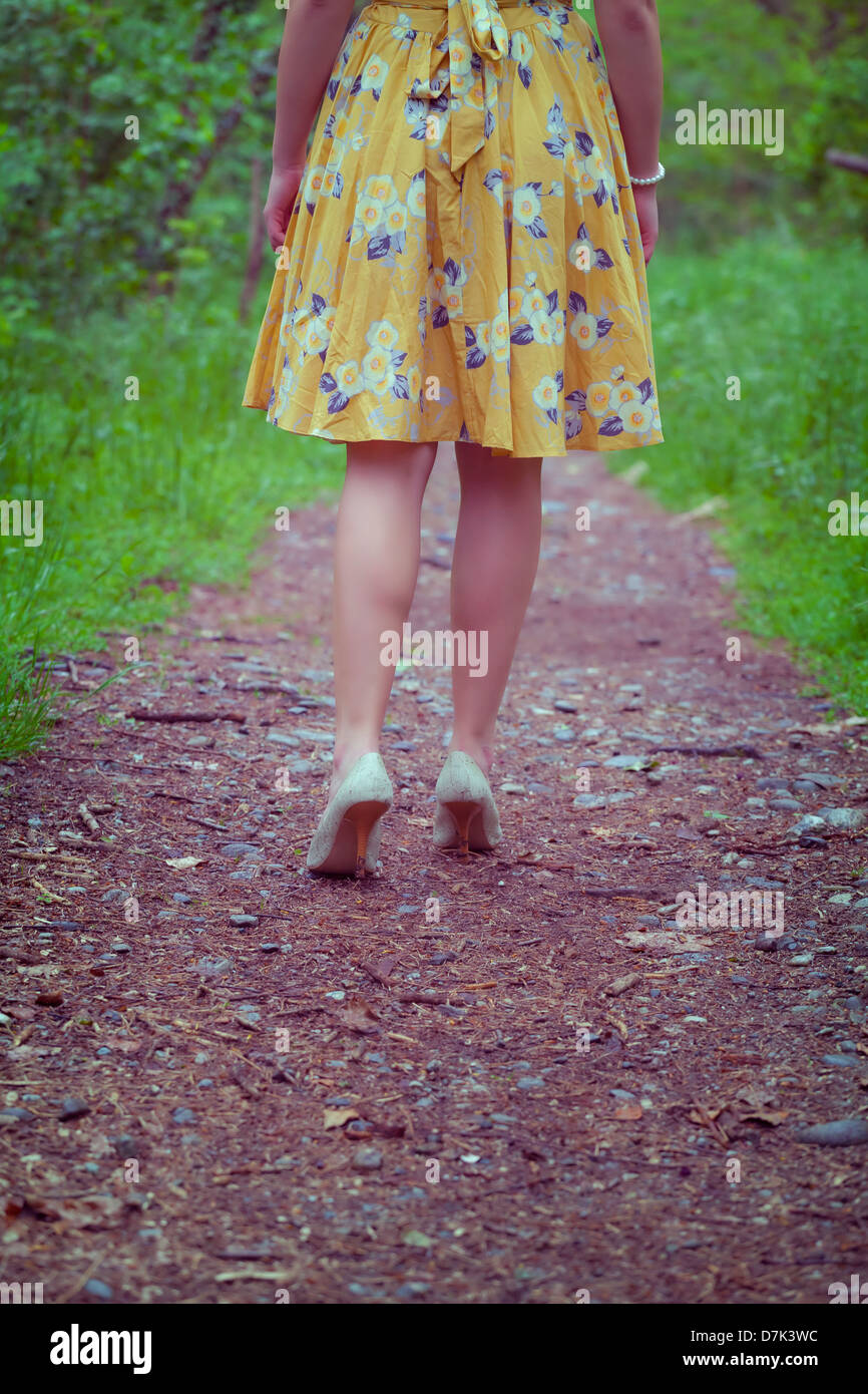 Les jambes d'une femme dans une robe jaune marche sur un sentier dans les bois Banque D'Images