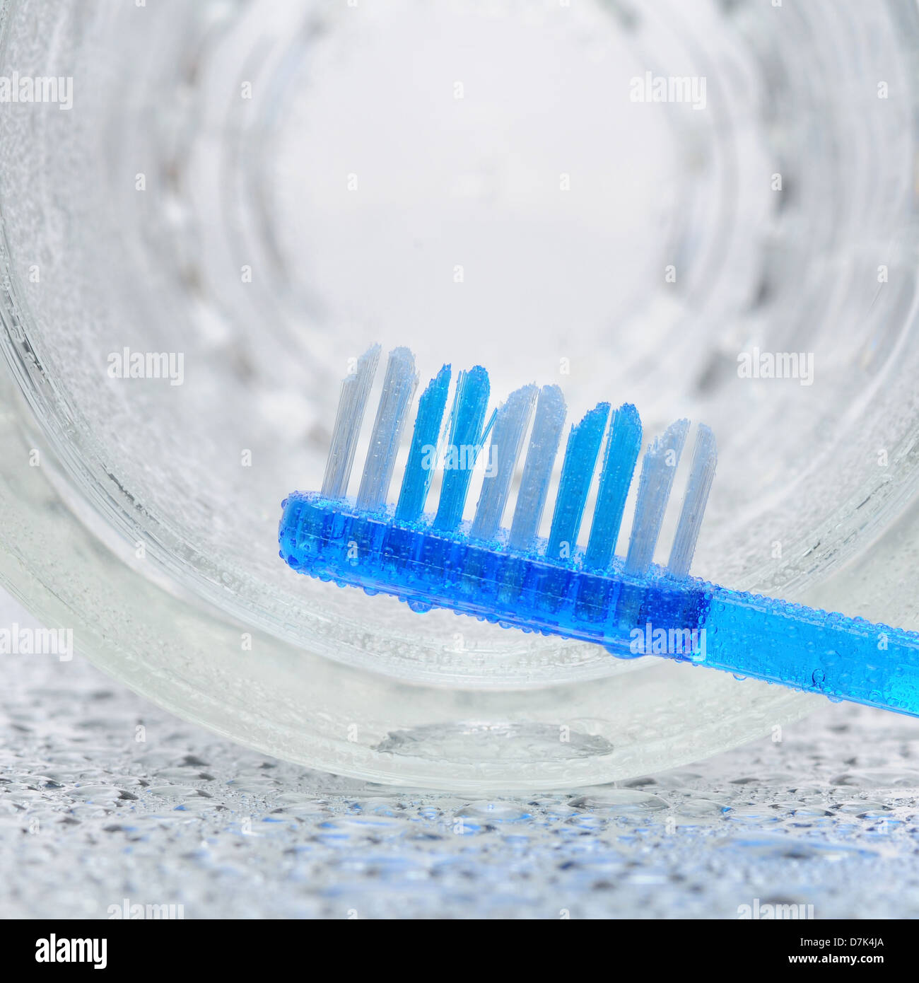 Une brosse à dents bleu portant sur un compteur de salle de bains humides avec un verre sur le côté à l'arrière-plan. Banque D'Images