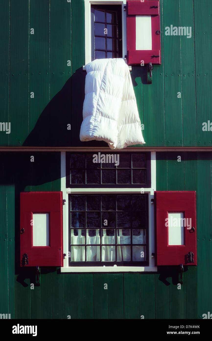 Une couette blanche sortir d'une fenêtre d'une maison en bois vert avec des volets rouges Banque D'Images