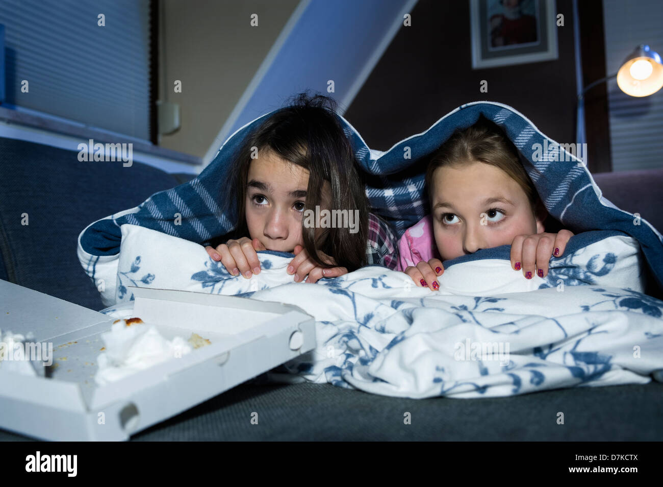 Les filles se cachant sous drap de lit tout en regardant un film effrayant Banque D'Images