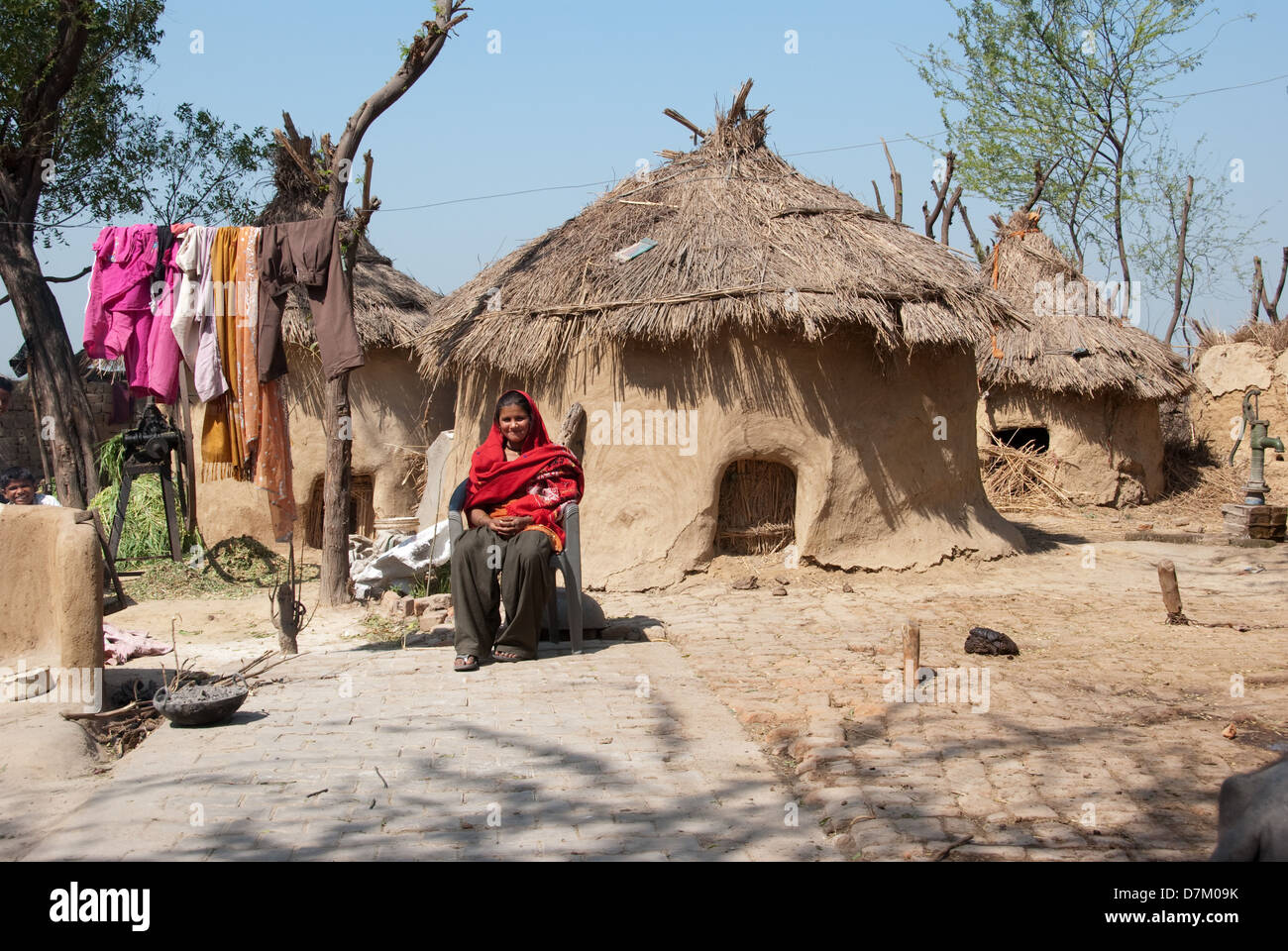 La vie du village est difficile, et lady prend un repos bien mérité à partir de tâches quotidiennes. Dans les communautés villageoises mesdames jouent un rôle majeur dans le maintien de la propriété familiale. Leur style de vie peut être beaucoup de main-d'oeuvre travaillant souvent du lever au coucher du soleil et au-delà. La bouse de buffle, mur, maison, dame président, corde, marron, rouge, bleu, toit de paille, côté cour intérieure, tube, bien Banque D'Images