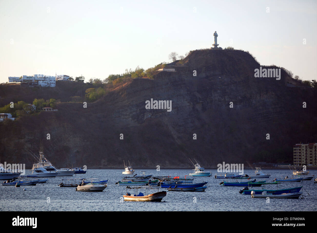 Le crépuscule s'installe au-dessus de San Juan del sur, Nicaragua, alors que les bateaux de pêche reposent dans le port sous une statue perchée au sommet d'une colline. Banque D'Images