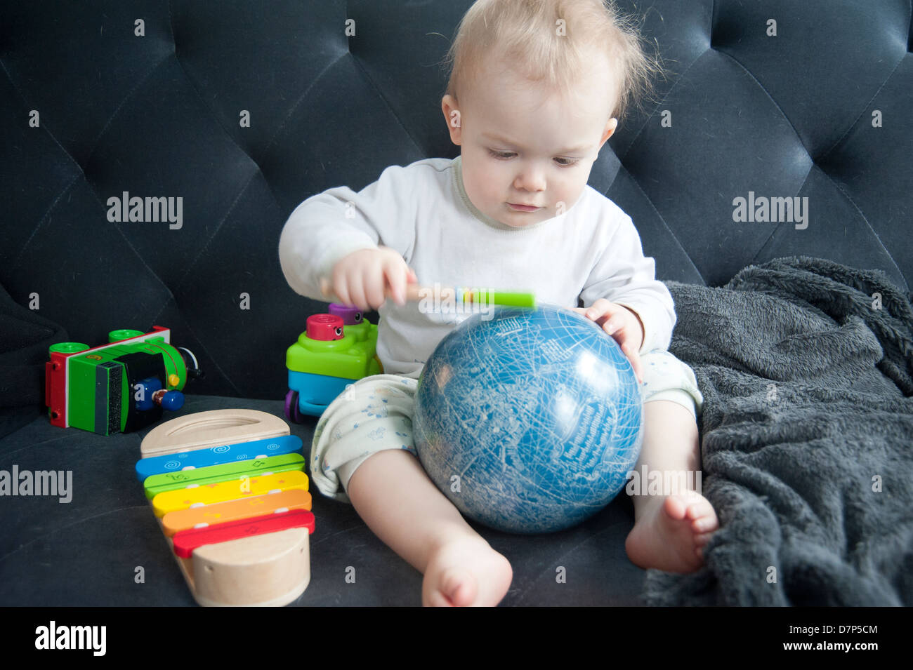 Baby sitting sur le canapé entourée de jouets, mais frapper sur un globe Banque D'Images