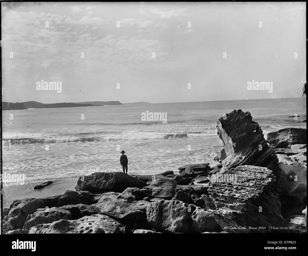 Cette photographie en noir et blanc capture Curl Curl Beach, située à Manly, en Nouvelle-Galles du Sud. L'image, conservée au Henry Powerhouse Museum, met en valeur le littoral et les vagues tranquilles, reflétant la beauté naturelle de la côte australienne. Banque D'Images