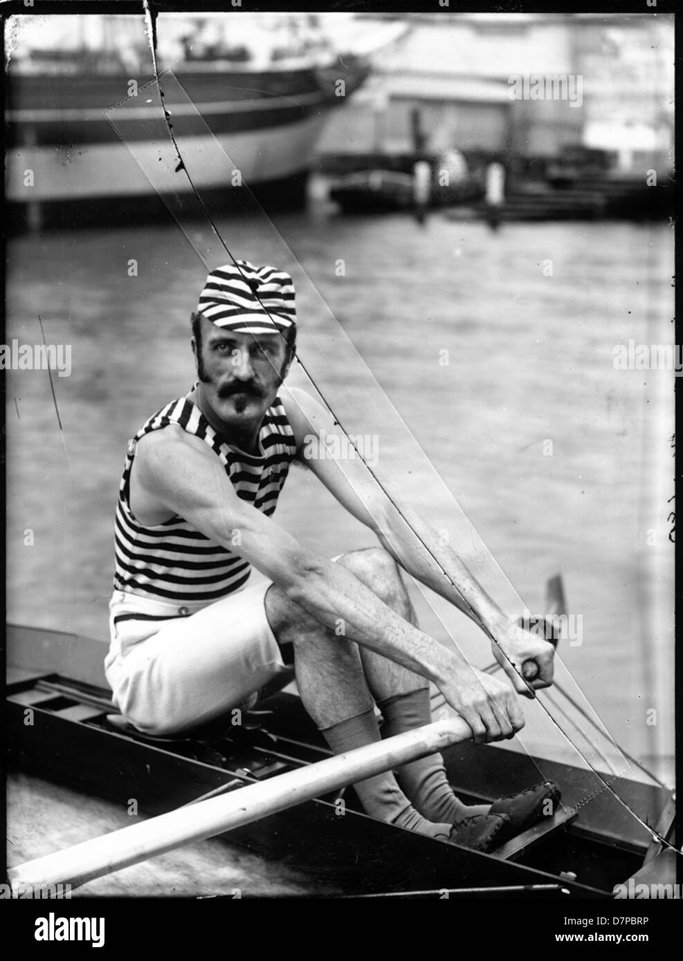 Cette photographie en noir et blanc capture Frank Senior, un sculleur, lors d'un événement d'aviron. L'image, conservée dans le Powerhouse Museum, met en évidence l'intense concentration de Senior alors qu'il rentre, portant une chemise rayée et une moustache, une relique de l'ère vintage de l'aviron de compétition. Banque D'Images