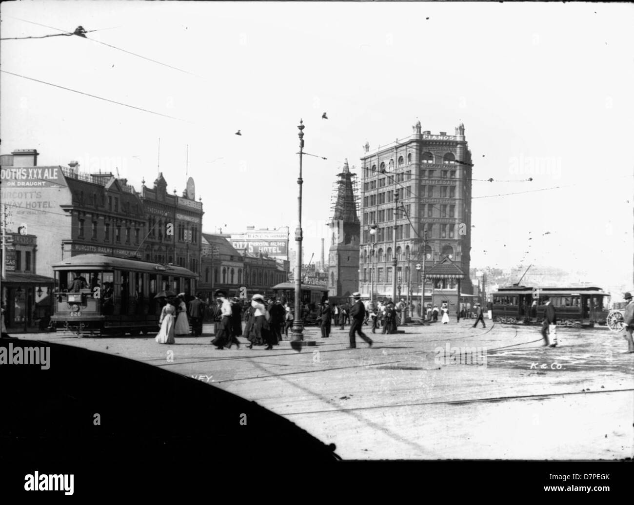 Cette image représente Railway Square à Sydney, mettant en valeur le Murcott's Railway Hotel et la Christ Church voisine de Laurence. La scène historique comprend des fils aériens, avec le Powerhouse Museum répertorié pour référence. La région fait partie du paysage urbain en pleine évolution de Sydney, autrefois centre de transport et d'hospitalité. Banque D'Images
