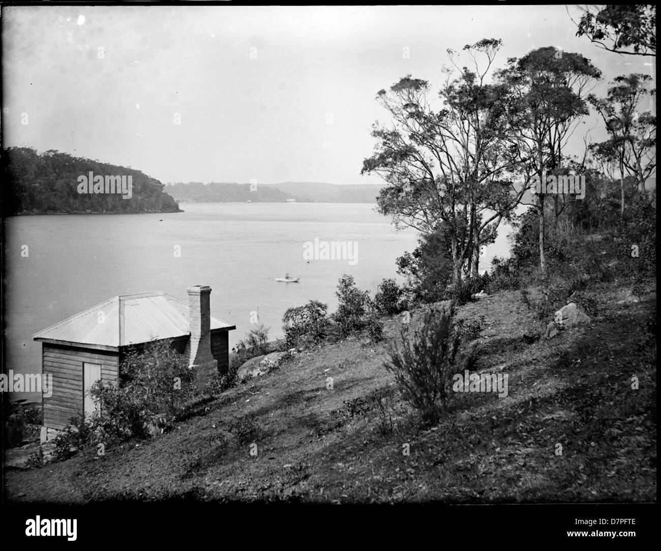 Une photographie historique du port de Sydney, avec une cabane en briques au premier plan, capturant une vue panoramique sur l'eau et le paysage environnant. L'image comprend des éléments comme le fer ondulé et les eucalyptus, reflétant la vie du début du XXe siècle en Australie. Banque D'Images