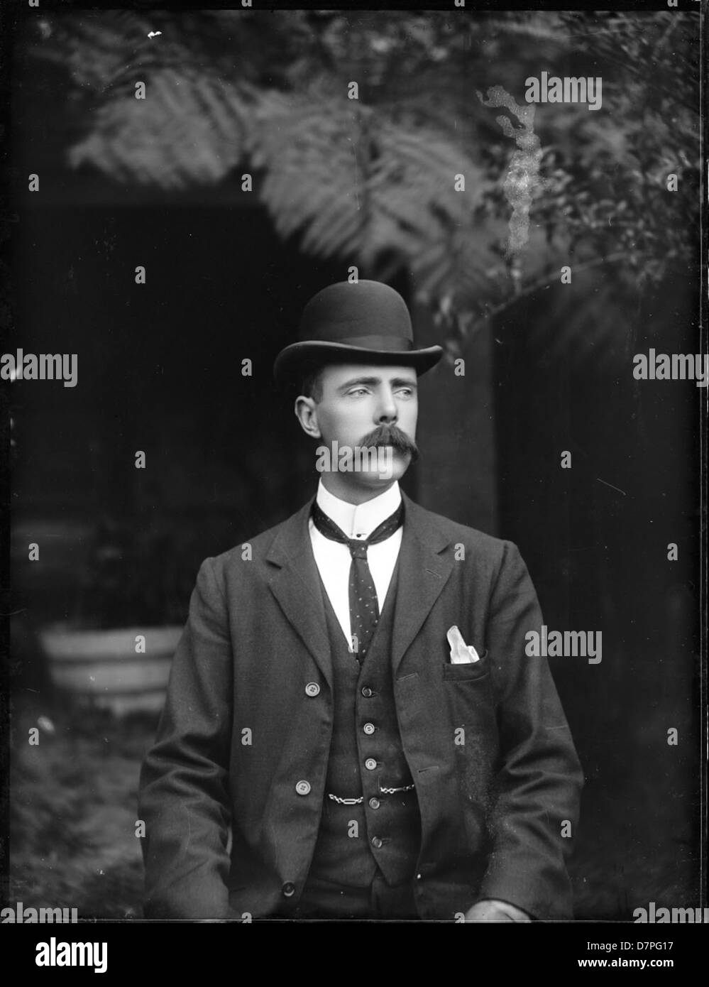Portrait d'un homme de l'époque édouardienne, vêtu d'un costume avec un gilet, avec un chapeau melon, une moustache, une cravate et une chaîne porte-clés. Cette image vintage capture le style élégant de l'époque, mettant l'accent sur les accessoires classiques et la tenue habillée. Banque D'Images