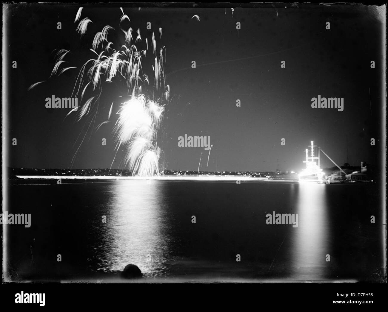 Cette image vibrante de feux d'artifice au-dessus d'un port capture l'esprit festif, probablement dans le port de Sydney, avec un contraste de lumières vives sur le ciel nocturne. La photographie est conservée au Powerhouse Museum, documentant des événements emblématiques. Banque D'Images