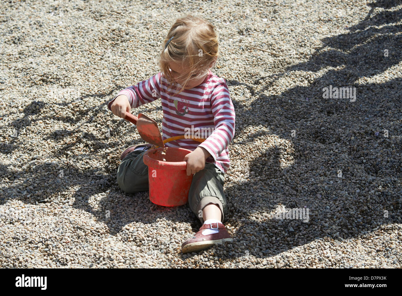 Blonde yeux bleu enfant bébé fille 2 ans jouant avec des pierres et des cailloux en plein air sur l'aire de jeux Banque D'Images