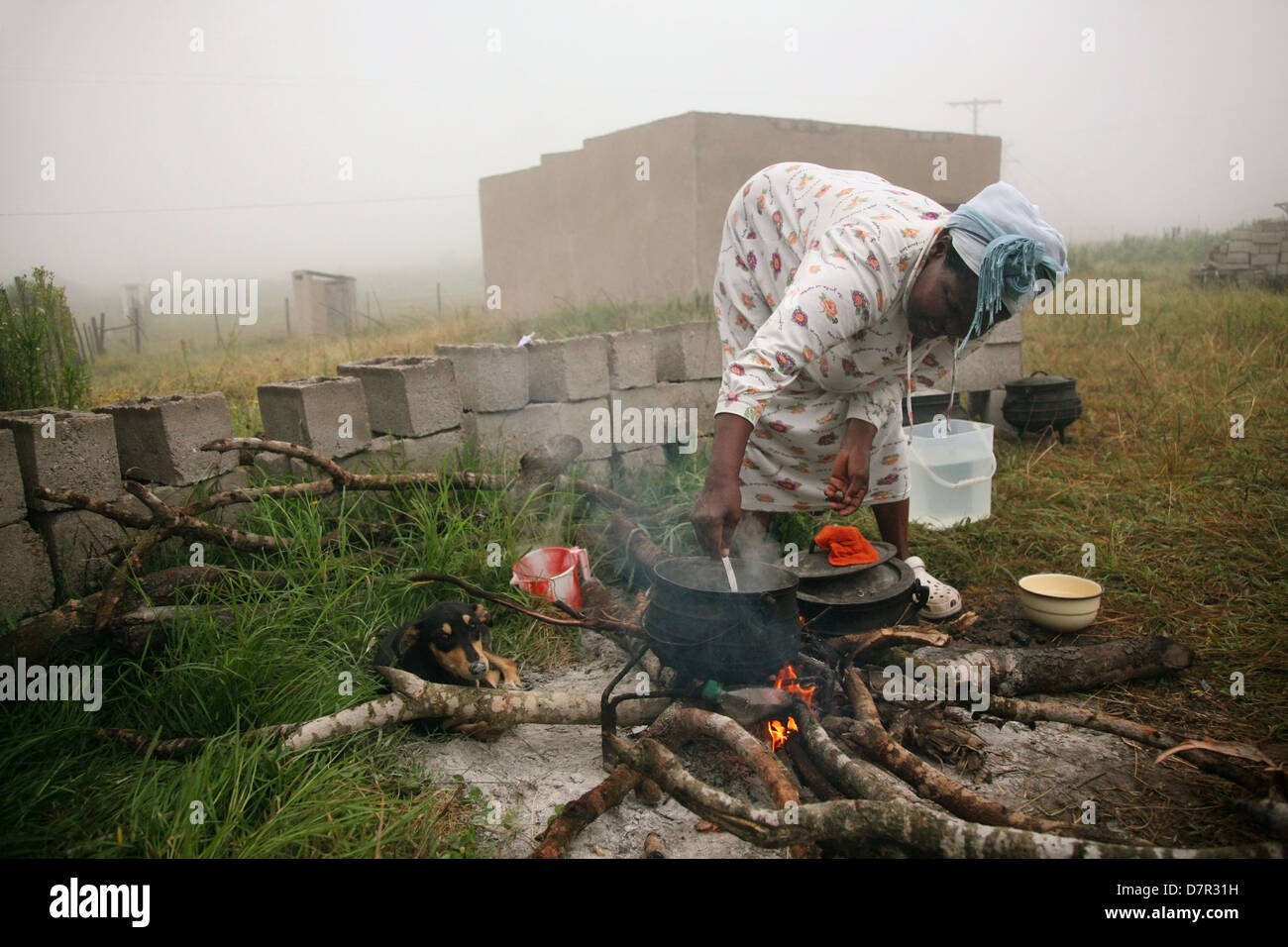 Une femme africaine cuisiniers à l'extérieur sur un feu de bois comme la brume en rouleaux Banque D'Images