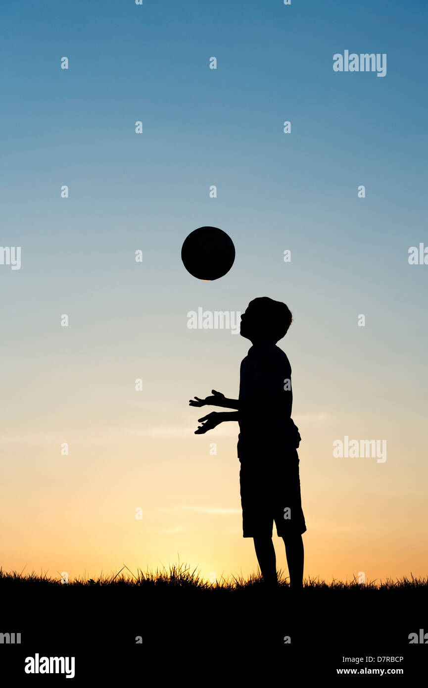 Garçon jouant avec un foot au coucher du soleil. Silhouette Banque D'Images