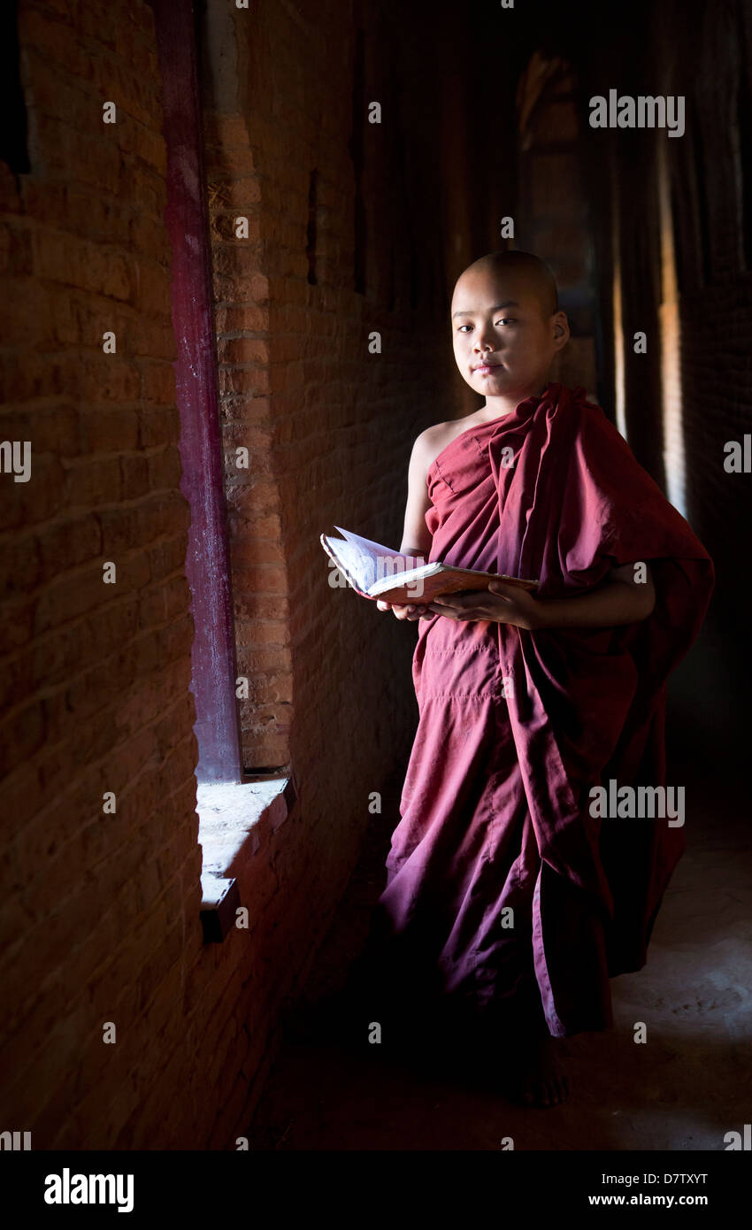 Moine Bouddhiste Novice écritures bouddhistes de lecture à la lumière d'une fenêtre dans l'un des nombreux temples de Bagan, Birmanie Banque D'Images