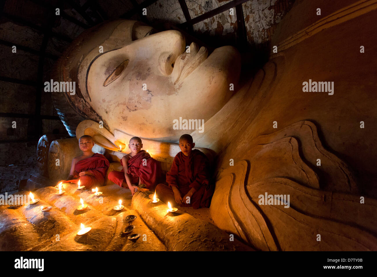 Trois moines bouddhistes novice assis par un grand bouddha couché dans la lumière des bougies, près de Shwesandaw Paya, Bagan, Birmanie Banque D'Images