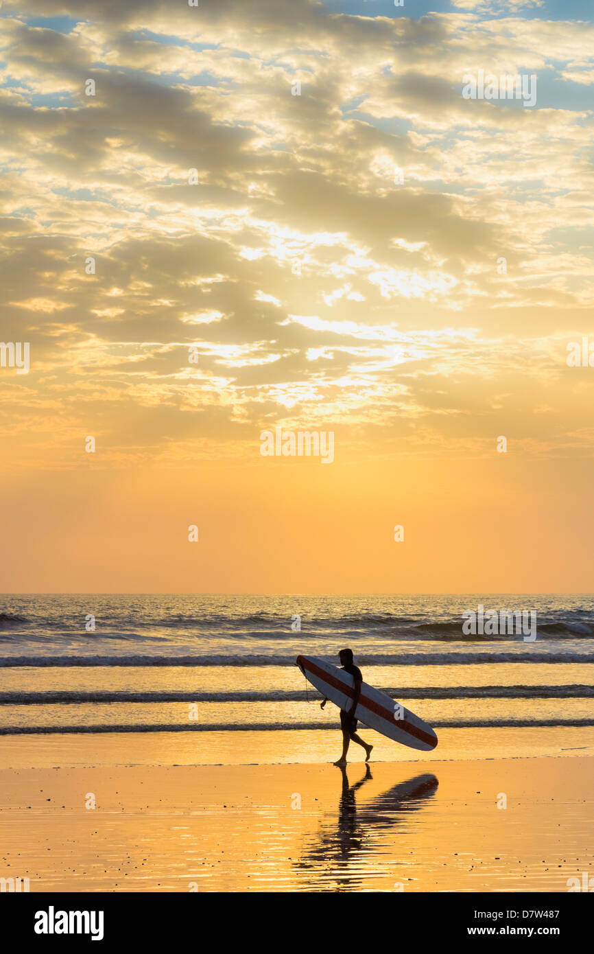 Surfer avec long bord au coucher du soleil sur la plage de surf populaire de Playa Guiones, Nosara, Péninsule de Nicoya, Province de Guanacaste, Costa Rica Banque D'Images
