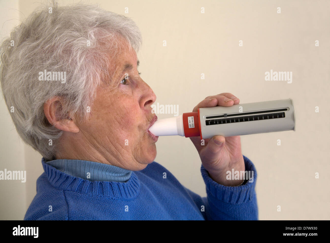 Femme âgée du Royaume-Uni avec des symptômes d'asthme soufflant dans le flux de pointe appareil de mesure pour surveiller la capacité pulmonaire Banque D'Images