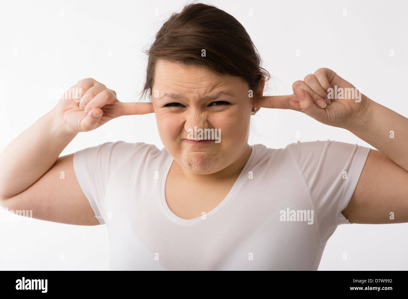 Une jeune brunette young Caucasian girl avec ses doigts dans ses oreilles de tenir à l'écart du bruit retentit Banque D'Images