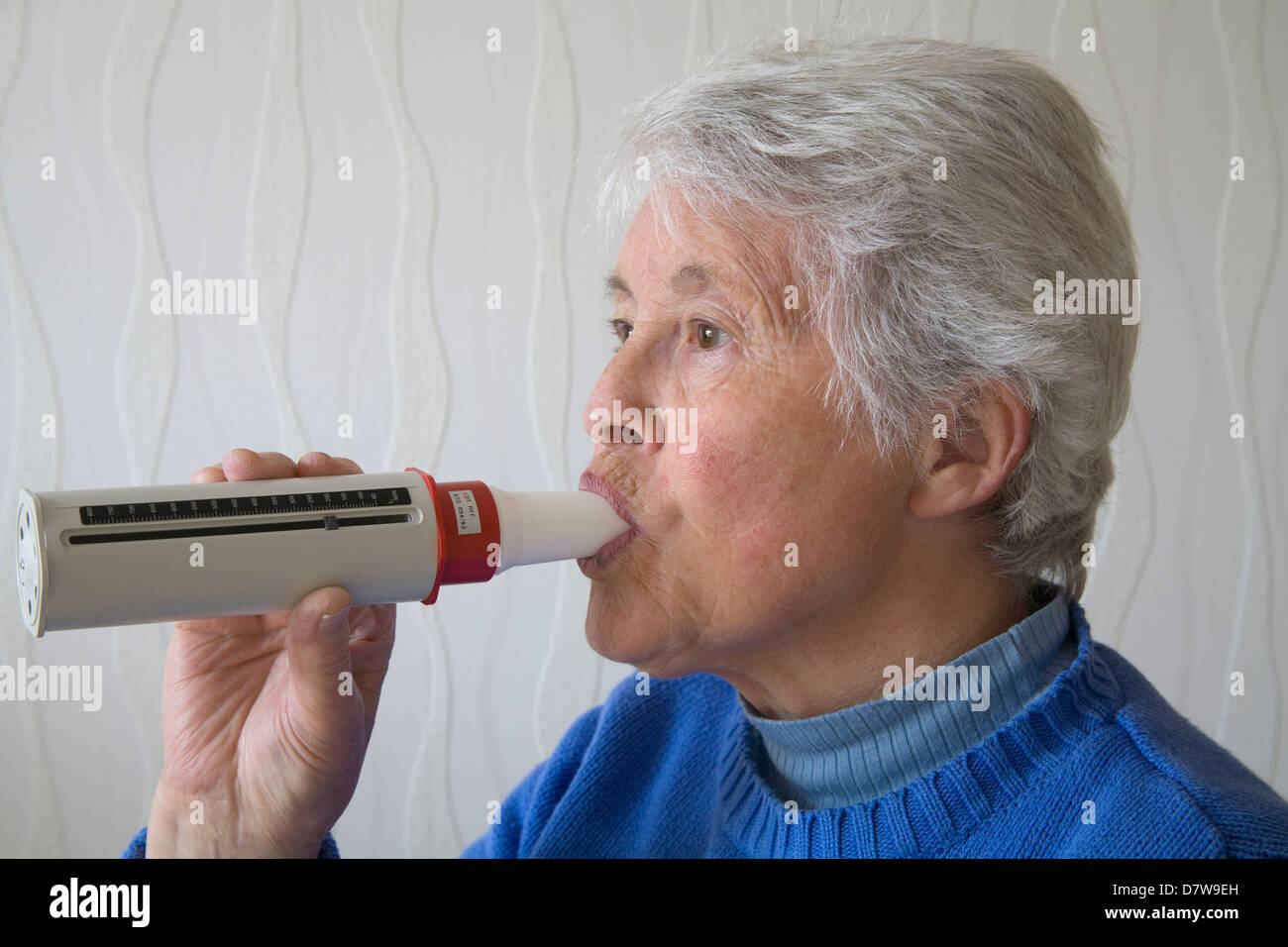 UK femme âgée soufflant dans débitmètre de pointe pour surveiller la capacité pulmonaire Banque D'Images