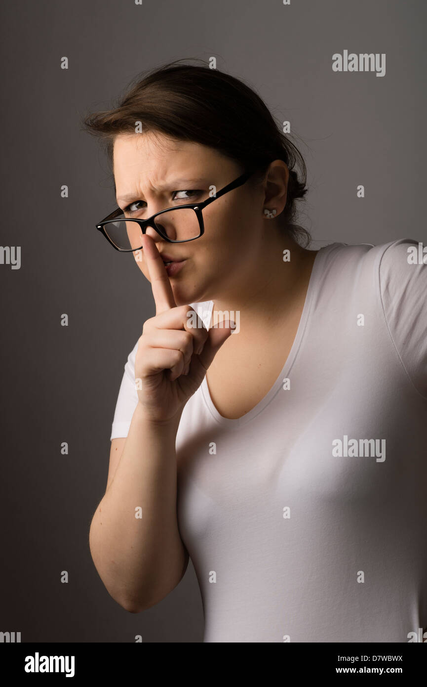 Une jeune brunette young woman wearing glasses avec son doigt sur ses lèvres, demandant le silence Banque D'Images