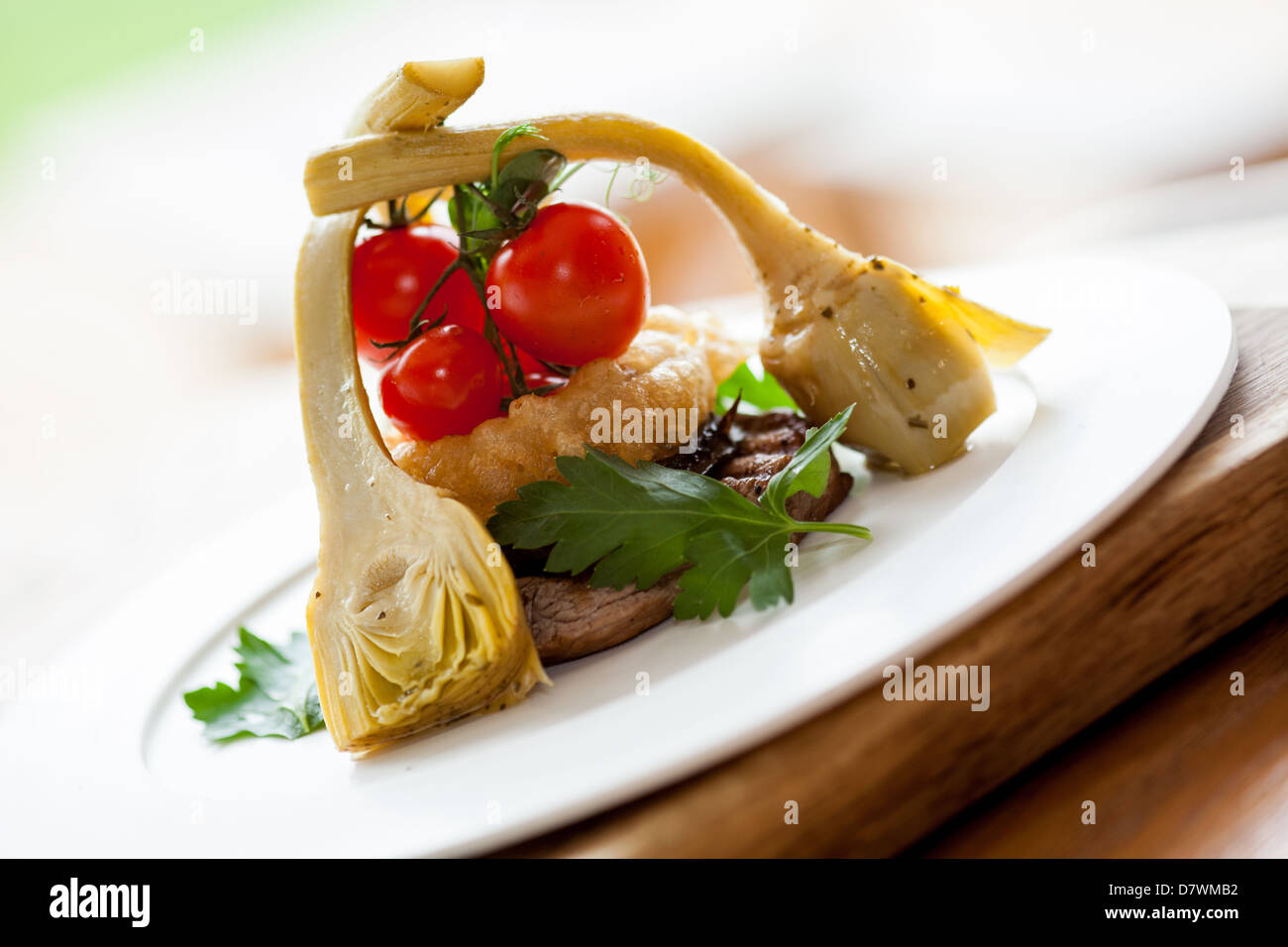 Steak de surlonge repas servi avec des artichauts, oignons et tomates fraîches sur une plaque blanche sur un bloc de bois Banque D'Images