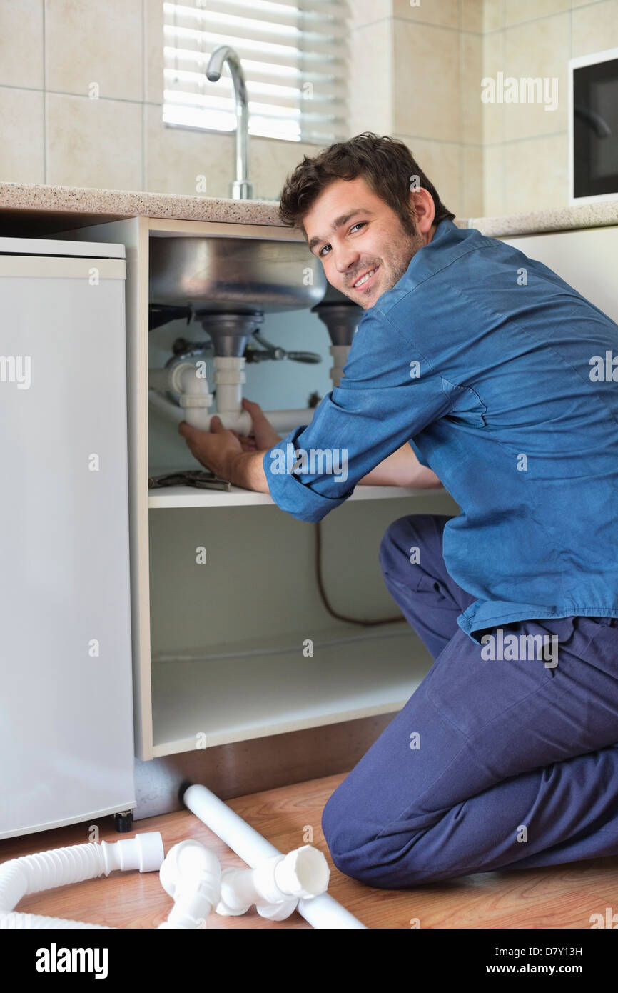 Plombier travaillant sur les tuyaux sous l'évier de cuisine Banque D'Images