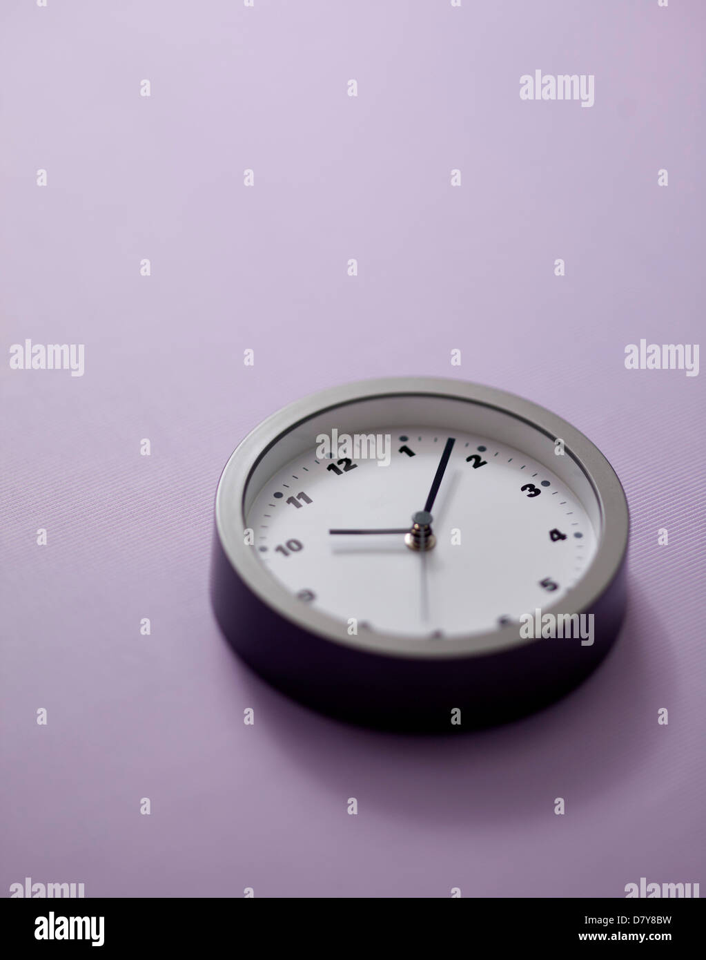 Une petite horloge murale sur un mur violet clair. Banque D'Images