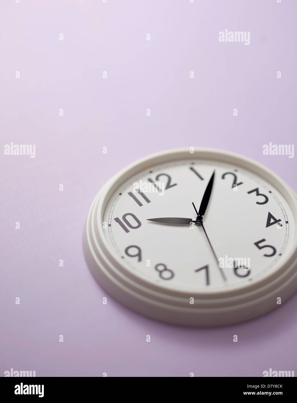 Une petite horloge murale sur un mur violet clair. Banque D'Images