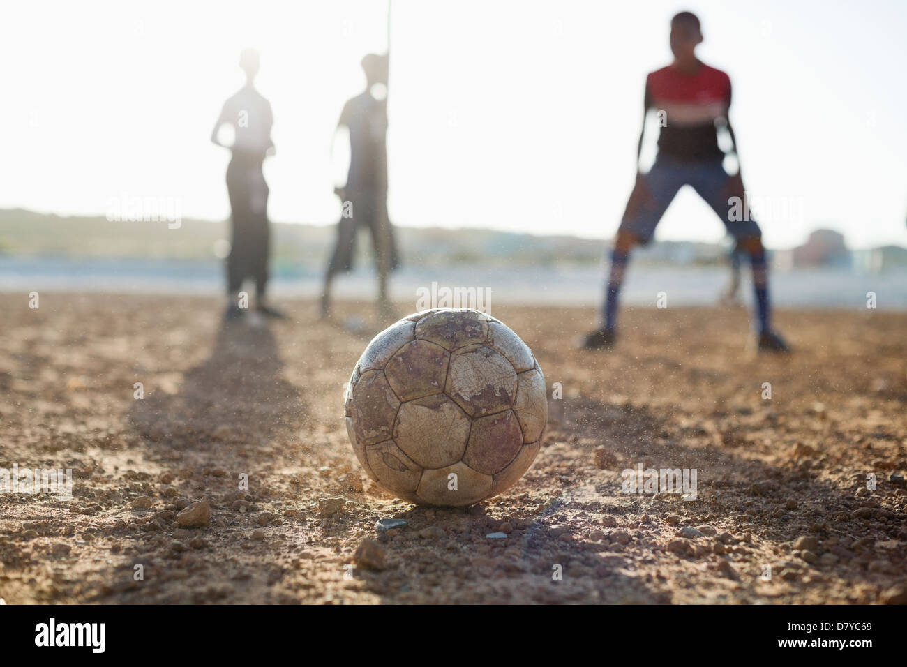 Boys playing soccer together in dirt field Banque D'Images