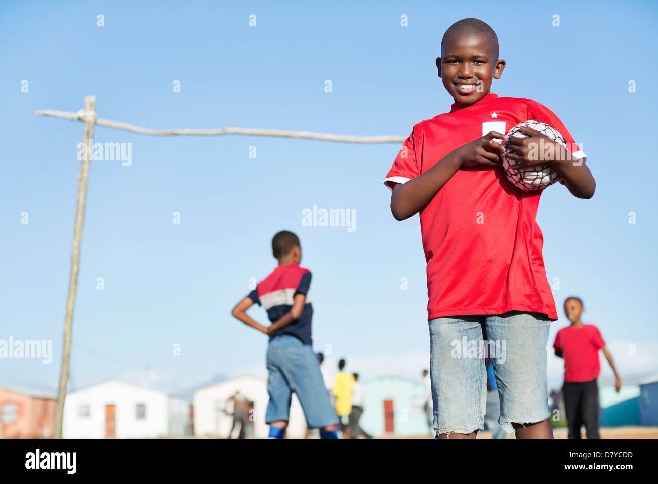 Boy holding soccer ball in dirt field Banque D'Images