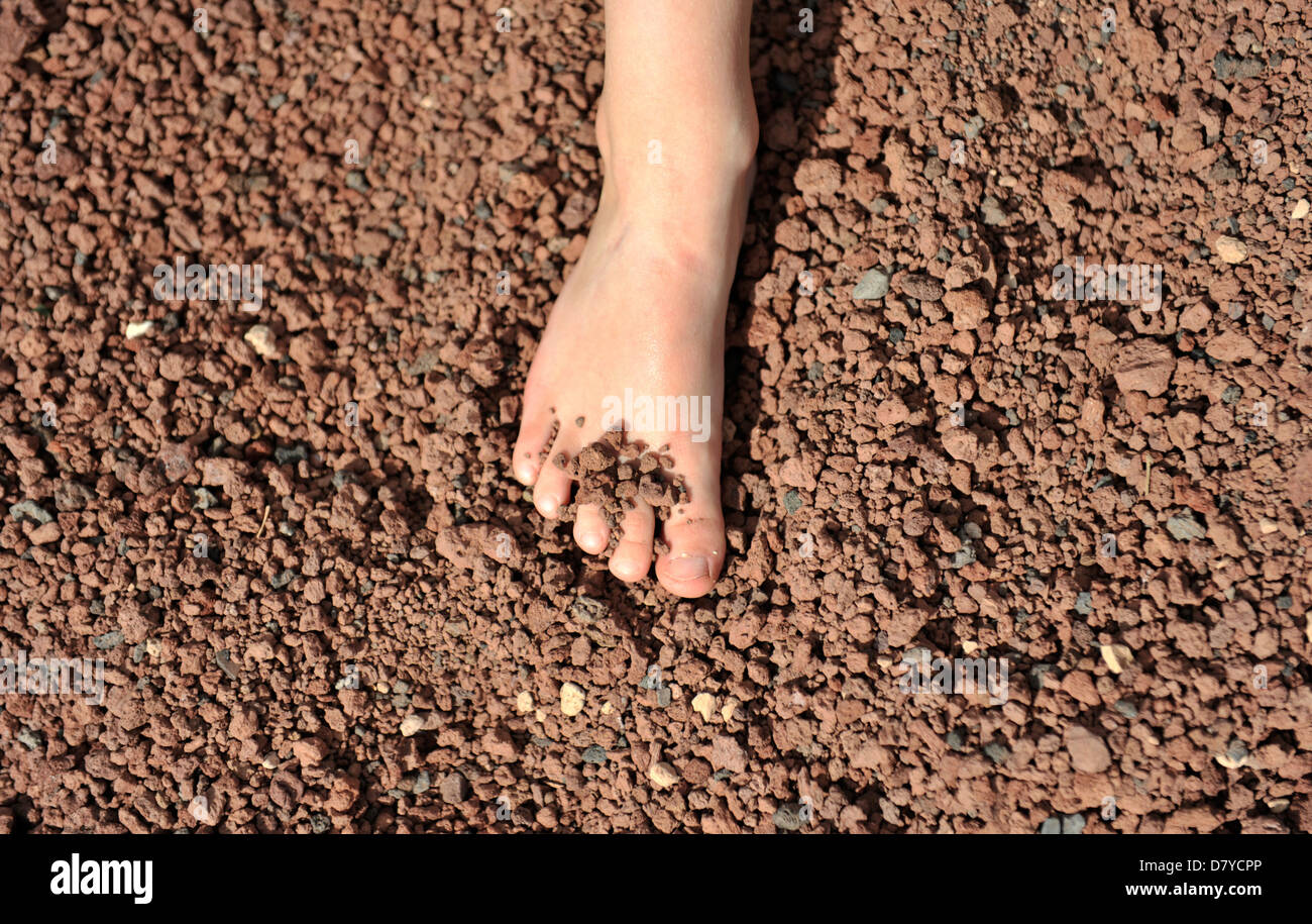 Le pied d'un enfant en gravier volcanique rouge, Lanzarote, îles Canaries. Banque D'Images