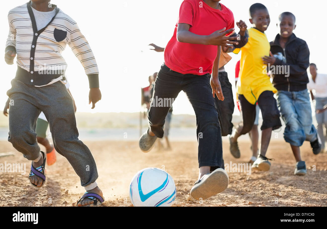 Boys playing soccer together in dirt field Banque D'Images