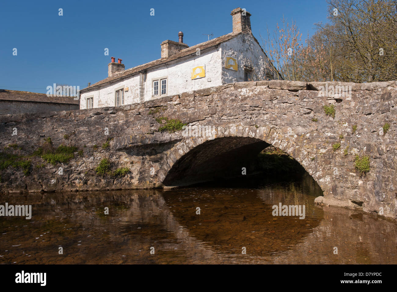 Pierre historique pont à travée unique au-dessus de l'eau Malham Beck dans le centre du pittoresque village de Dales sunny summer - Malham, North Yorkshire, Angleterre, Royaume-Uni. Banque D'Images