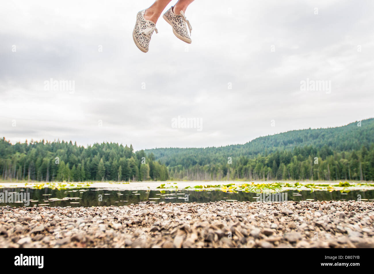 Une femme sautant à côté d'un lac dans la région de Bowen Island, British Columbia, Canada. Banque D'Images