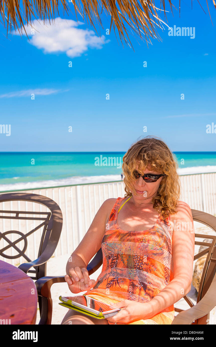 Femme de race blanche, 45, à l'aide de tablette iPad sur une plage de Floride, USA Banque D'Images