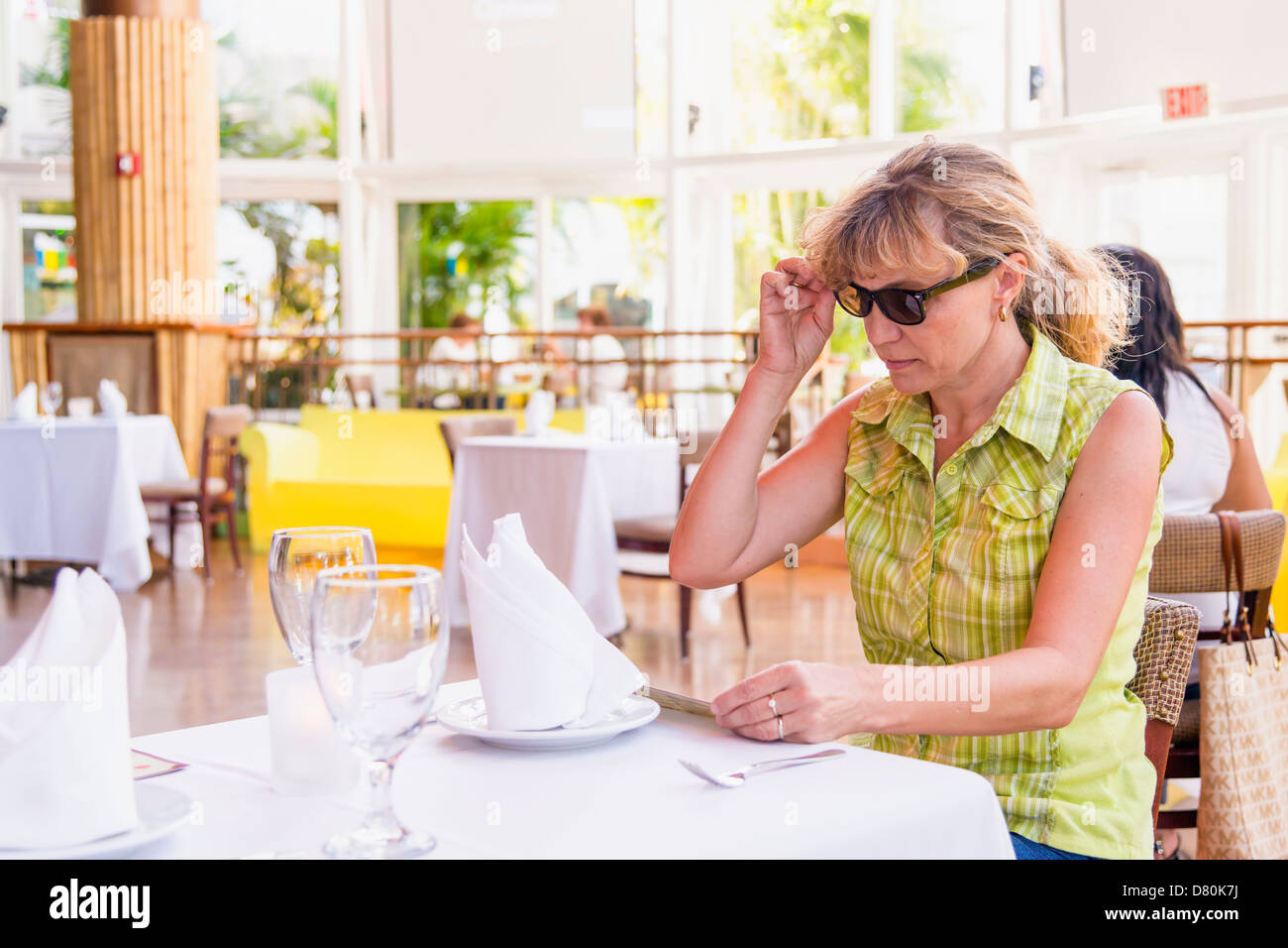 Femme de race blanche de 45 ans de prendre des lunettes de soleil hors de vérifier le menu dans un restaurant lumineux, léger, Miami, Floride, USA Banque D'Images