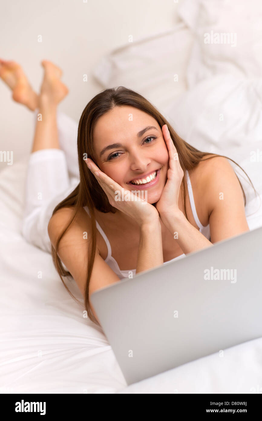 Attractive young woman at home working on laptop in bedroom Banque D'Images