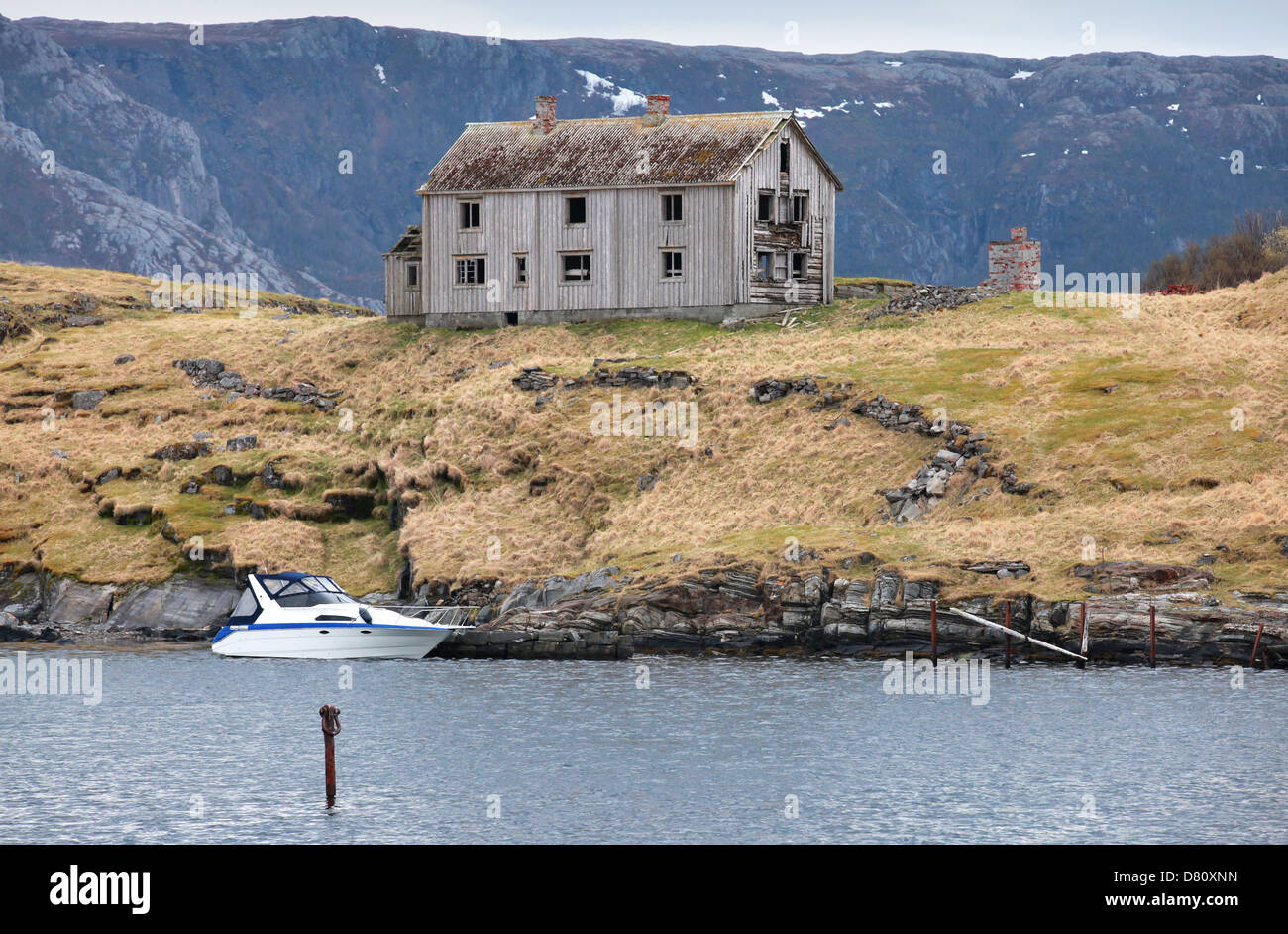 Ancienne maison en bois gris et petit bateau moderne sur le littoral en Norvège Banque D'Images